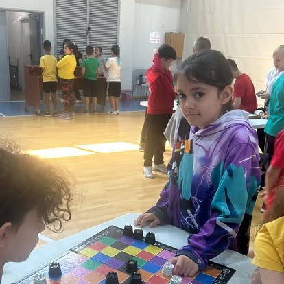 תלמידה מחייכת לצד משחק לוח צבעוני ביום פעילות