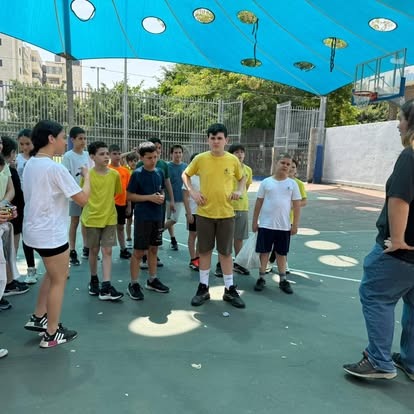 תלמידים מתכנסים במגרש הספורט החיצוני תחת גג בד