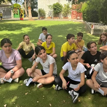 תלמידים יושבים על הדשא בפעילות חוץ עם דפי עבודה